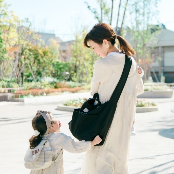 	黒いマザーズショルダーバッグを肩掛けしベビーカーを押すママと手をつなぐ女の子