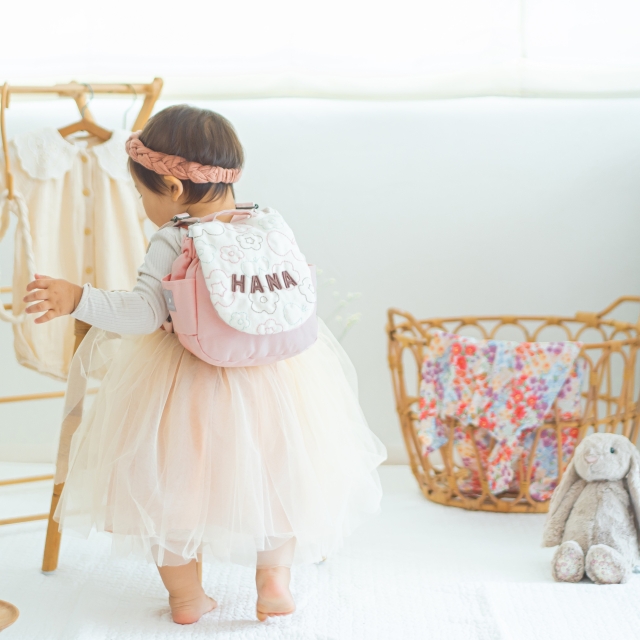 チュールワンピにおはなピンクの名入れリュックを背負う1歳女の子‐バースデーフォトに映える背中姿