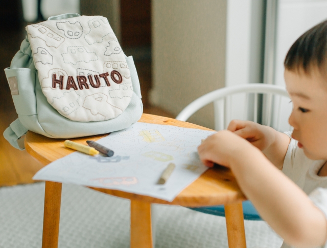 ミントグリーンのくるま名入れリュックをテーブルに置きお絵かきする男の子‐“好き”を背負うイメージカット