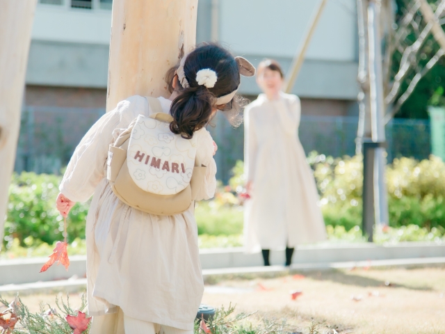 名入れベビーリュック〈おはな・ベージュ〉を背負った女の子が公園でママとかくれんぼ-1歳のお出かけシーンを彩るお絵かきステッチ着用イメージ