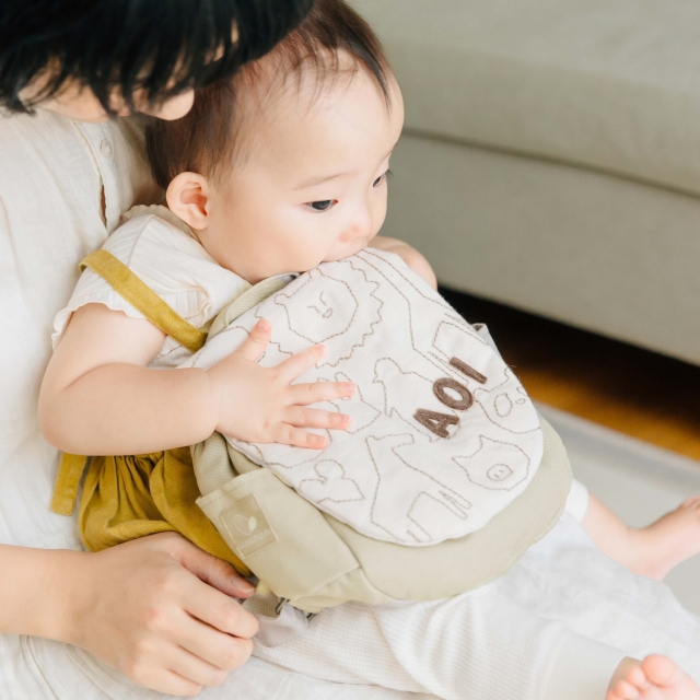ベージュのどうぶつ柄名入れリュックを抱えて遊ぶ0歳ベビー‐ふっくら刺繍の質感がわかるアップ