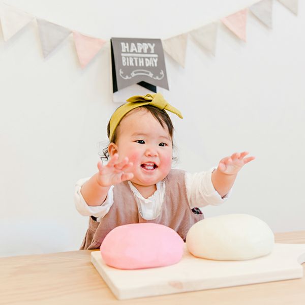 一升餅に手を伸ばす１歳女の子　ファーストバースデーの背負い餅シーン